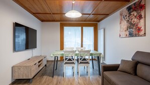 A cozy living room with a wooden ceiling, a dining table with chairs, a sofa, and a TV mounted on the wall. - New apartment in the center of Canazei (Canazei)