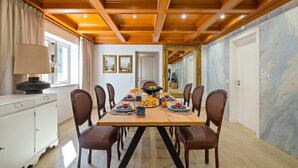 A dining area with a wooden table set for breakfast, surrounded by chairs, with a white cabinet and a lamp on the left. - Villa Rosa Estoril Retreat by Portugal Portfolio (Estoril)