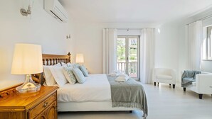 A hotel room with a bed, two bedside lamps, a wooden nightstand, a white armchair, and a view of the outdoors through a window. - Villa Rosa Estoril Retreat by Portugal Portfolio (Estoril)