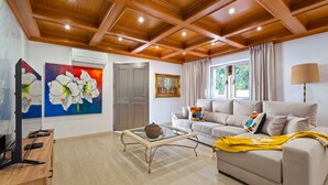 A living room with a wooden ceiling, a beige sofa, a glass coffee table, and artwork on the walls. - Villa Rosa Estoril Retreat by Portugal Portfolio (Estoril)