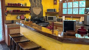 Une cuisine avec un mur jaune, un ventilateur de plafond, une enseigne représentant une tasse de café et une fenêtre donnant sur un beau paysage.