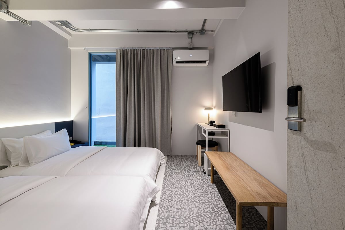 Quarto de hotel moderno com uma cama grande, uma escrivaninha, televisão de tela plana e uma janela com cortinas.