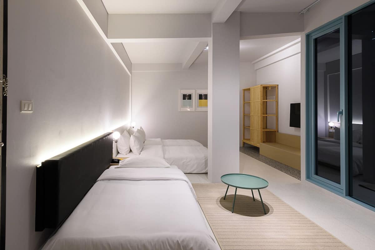 Quarto de hotel moderno com uma cama grande, uma mesa redonda pequena e uma porta deslizante que dá para uma varanda.