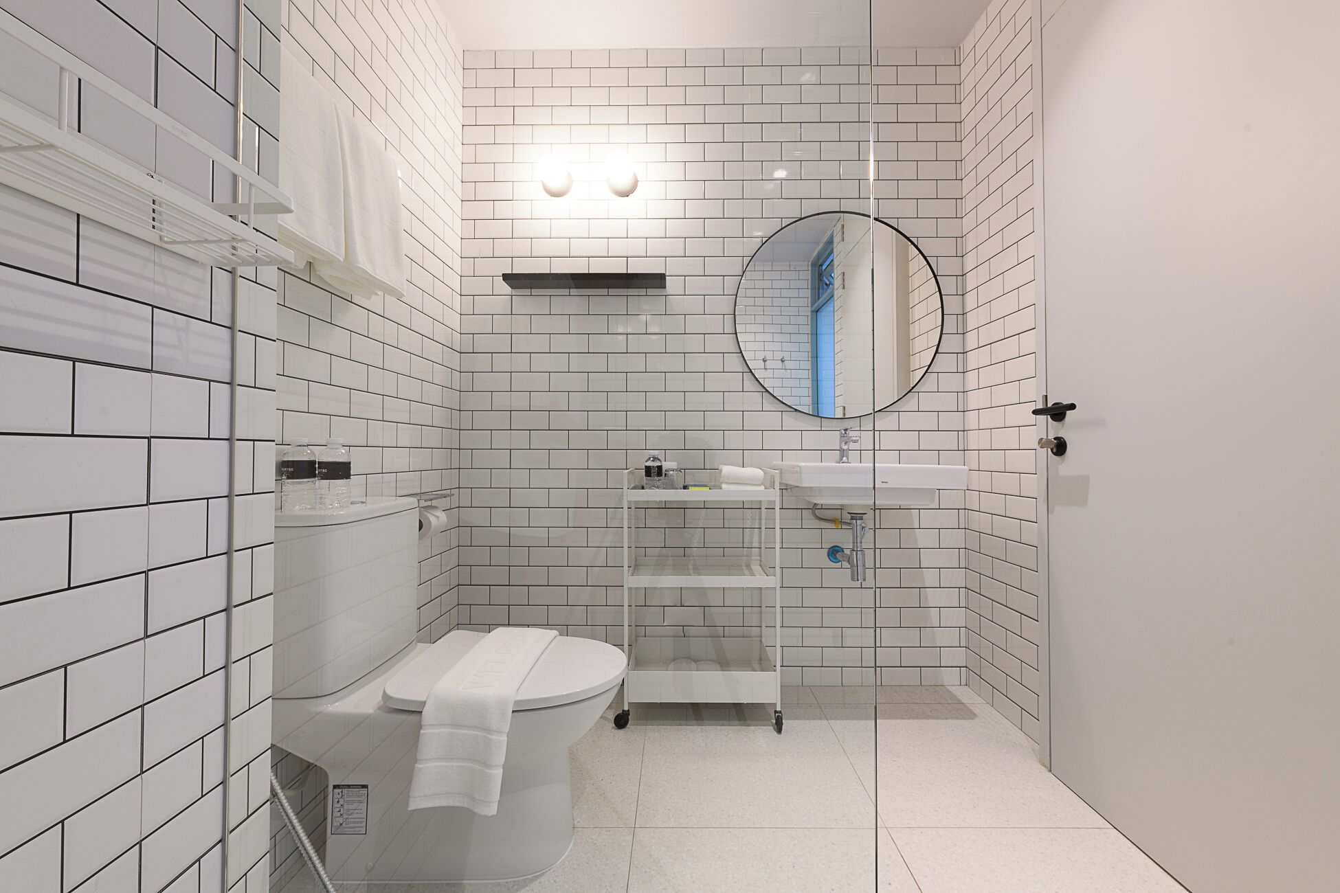 Et moderne badeværelse med hvide flisemur, toilet, håndvask og brusebad.