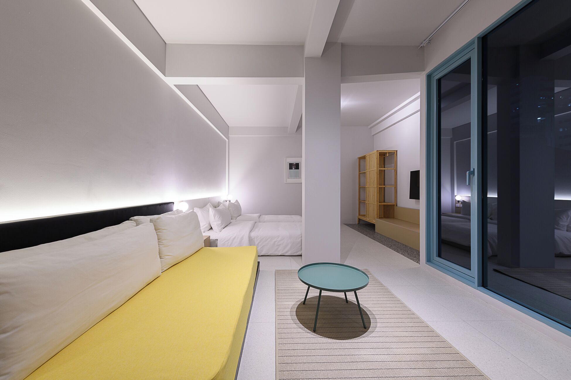 A modern hotel room with a yellow sofa, a small round table, and a large window.
