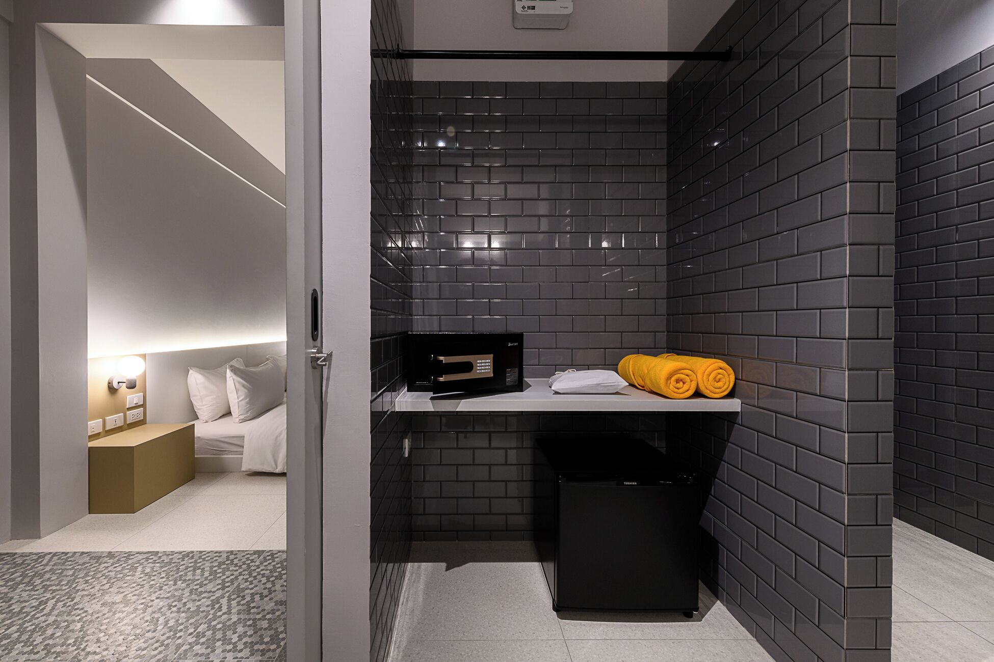 A compact bathroom with a black tiled wall, a small black trash bin, and a towel holder with yellow towels.