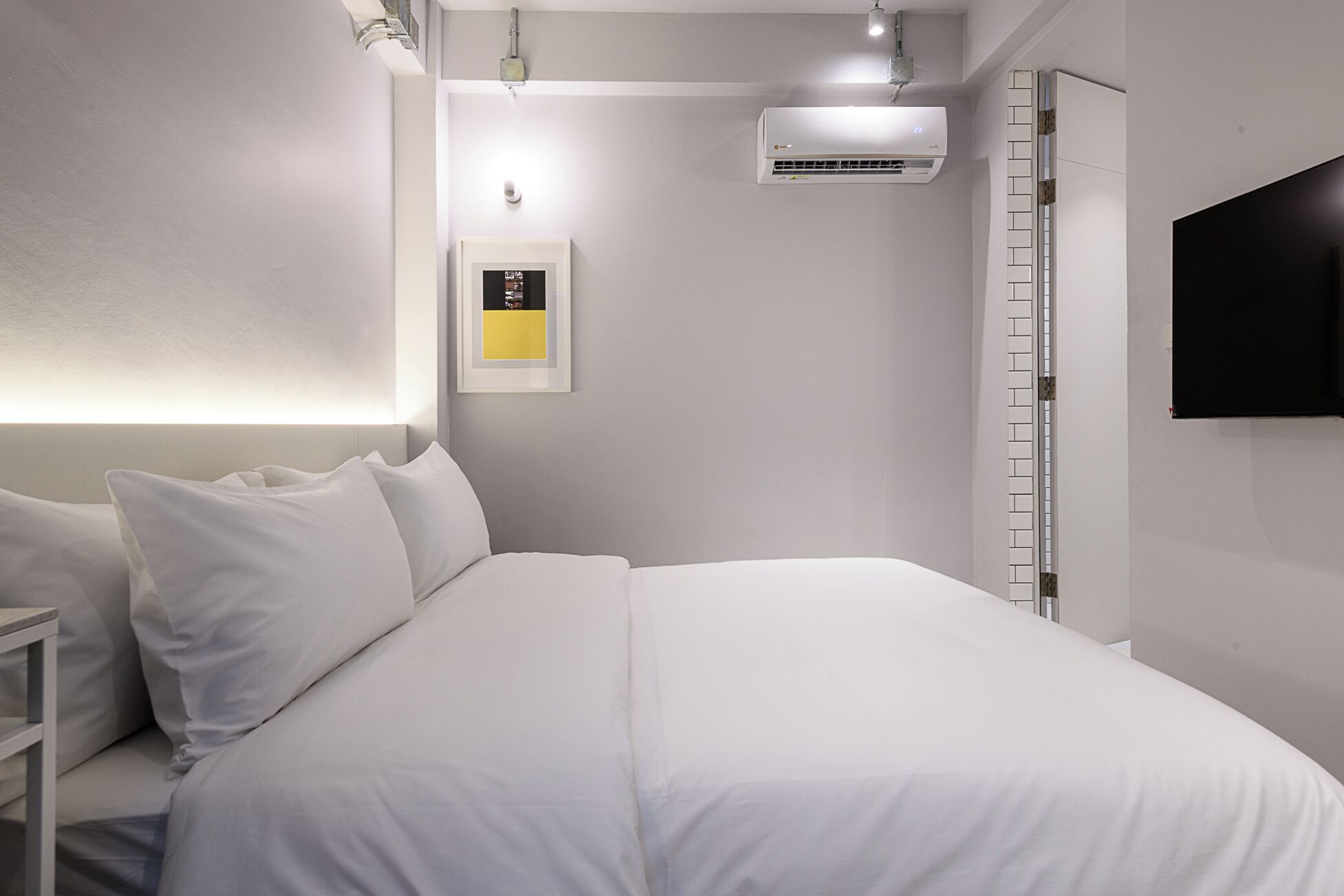 Una camera d'albergo moderna con un letto rifatto, una TV a parete e un condizionatore d'aria.
