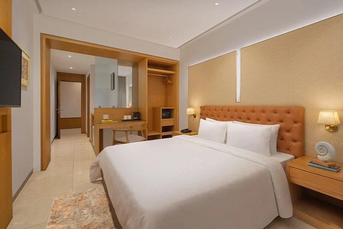 A hotel room with a large bed, a desk with a chair, a wardrobe, and a television.