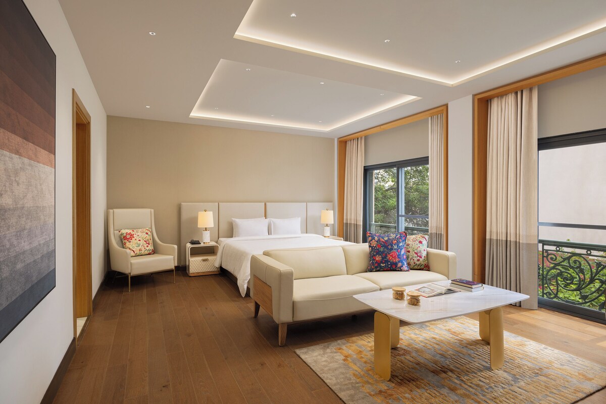A modern hotel room with a large bed, a sofa, a small table, and a nightstand.