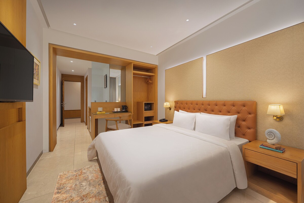 A hotel room with a large bed, a desk, a wardrobe, and a television.