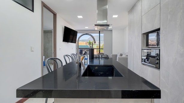 A modern kitchen with a central island, a built-in stove, and a large window offering a view of the outdoors.