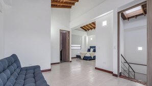 A spacious living area with a sofa, a staircase, and a bedroom visible in the background.