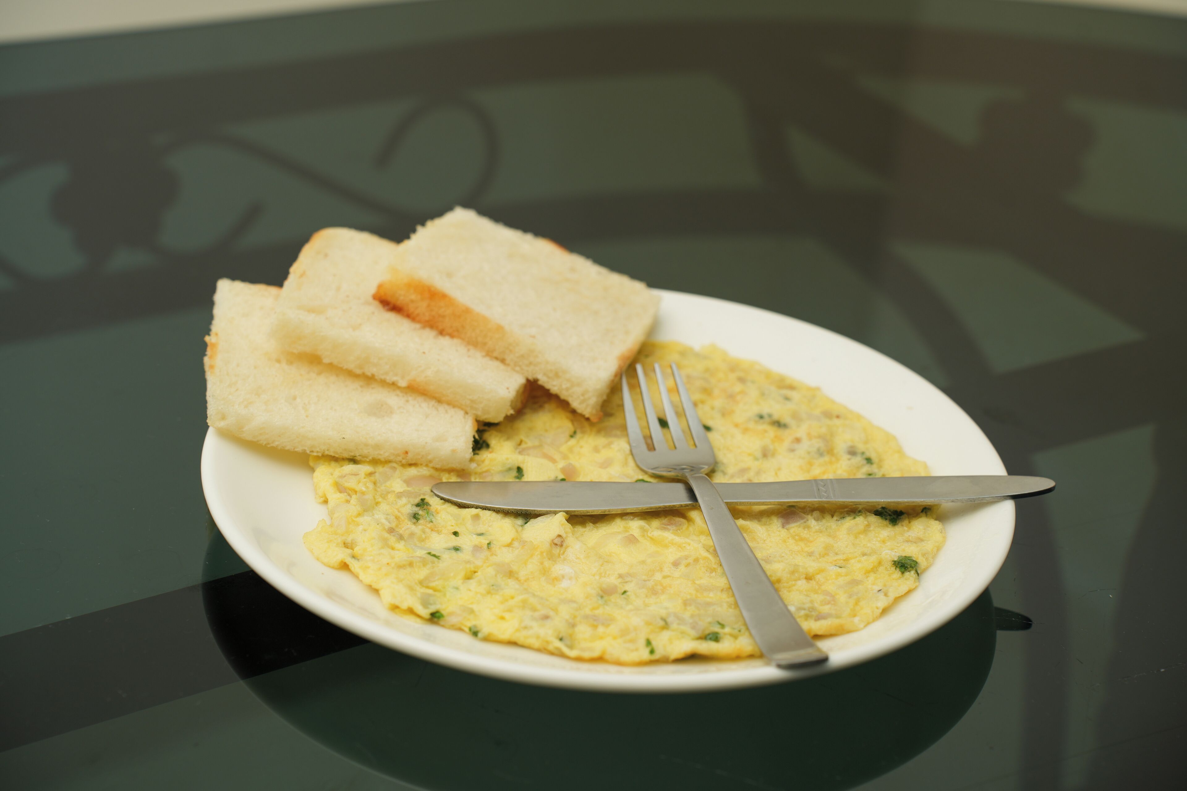 A plate with scrambled eggs and toast on a glass table.