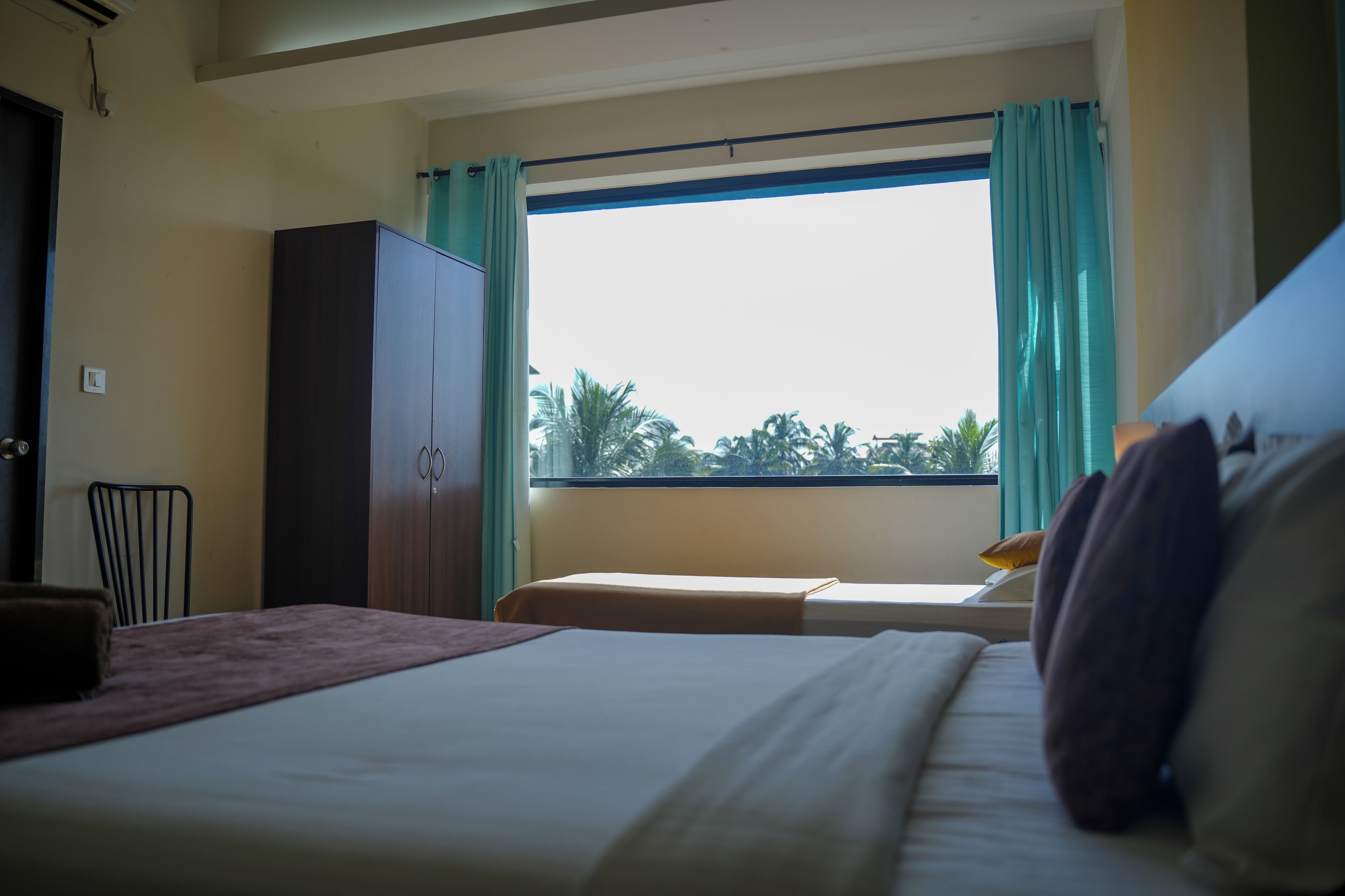 Quarto de hotel com cama, janela com cortinas, guarda-roupa e uma cadeira.