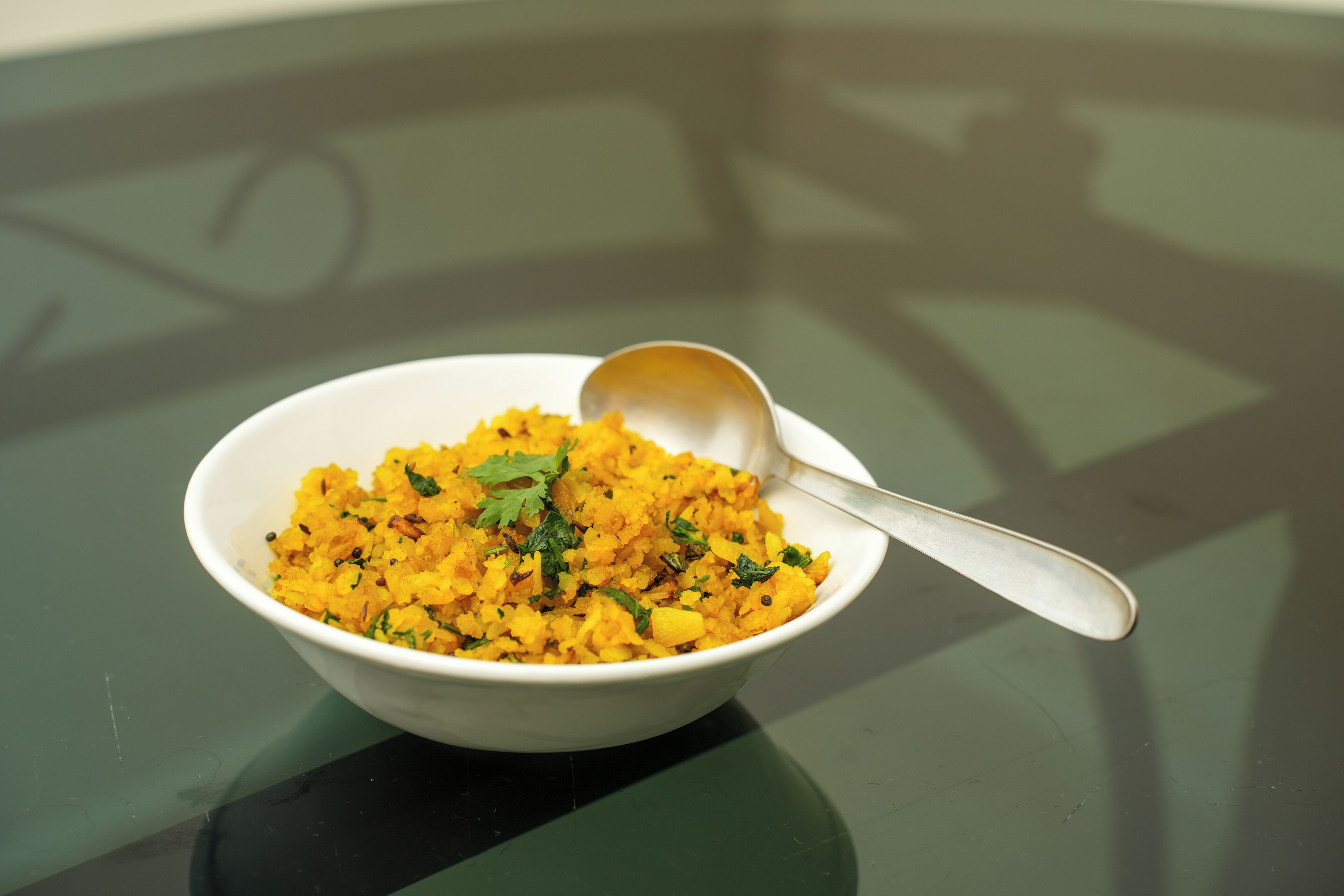 Un tazón de arroz amarillo adornado con hierbas sobre una superficie reflectante.