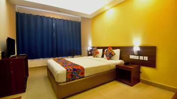A hotel room with a bed, bedside tables, a desk, a chair, a TV, and a window with curtains.