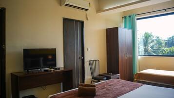 A hotel room with a bed, a desk with a TV, a wardrobe, and a window with a view of greenery.