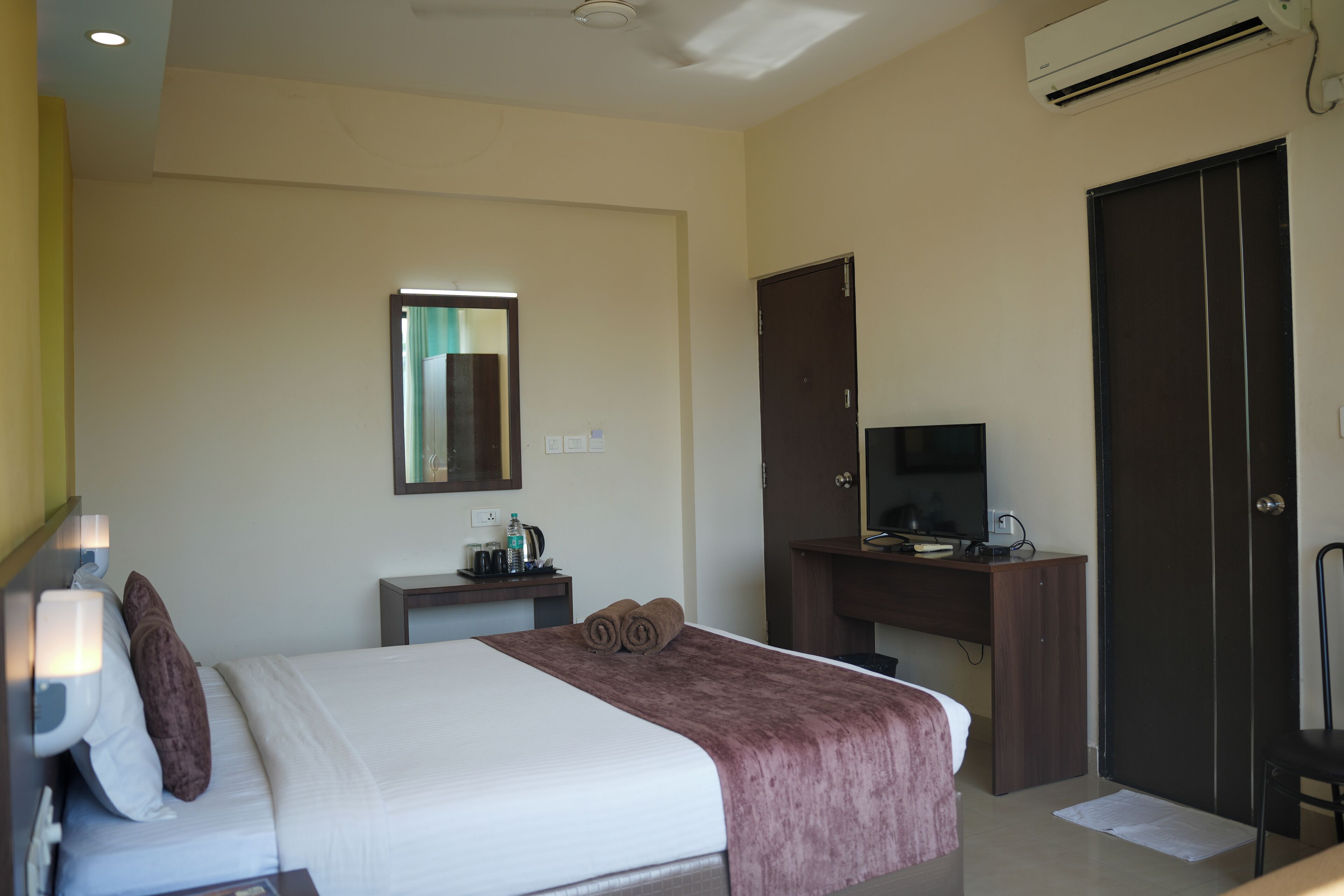 A hotel room with a bed, a desk with a computer, a TV, and a wardrobe.
