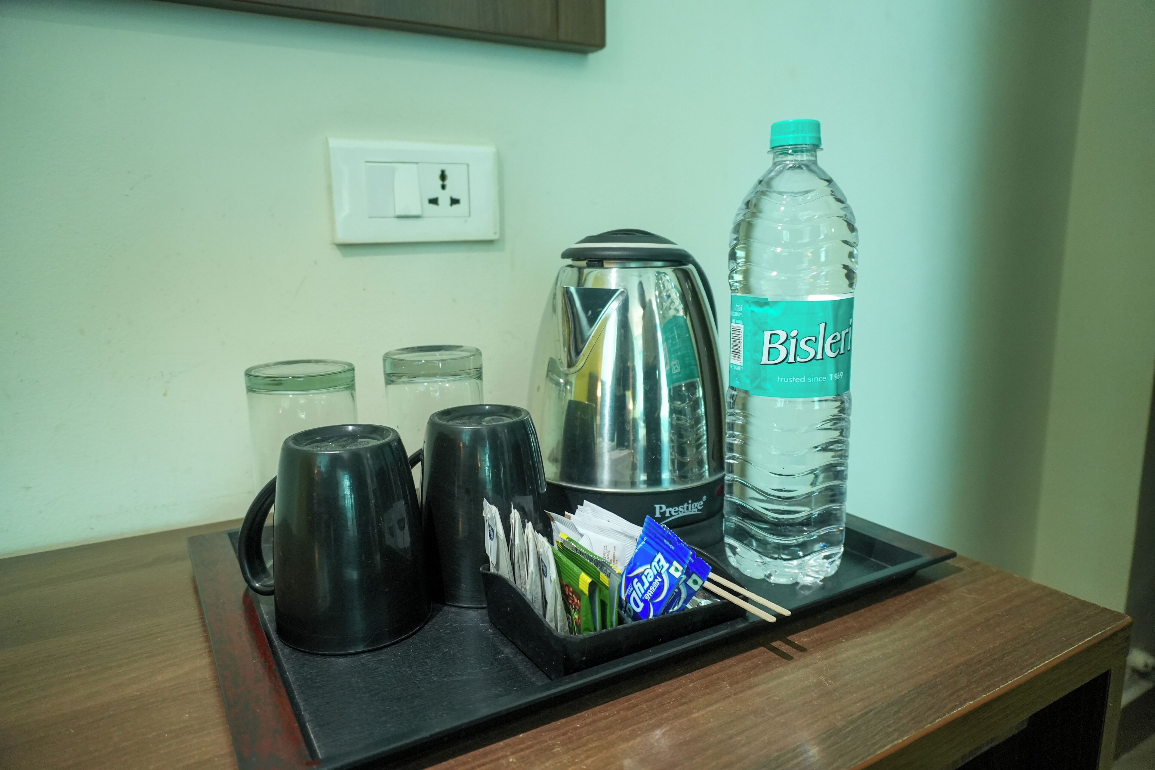 A tray with a Bisleri water bottle, a Prestige coffee maker, and several cups on a wooden table.