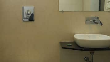 Un baño con inodoro, lavamanos, espejo y una ventana sobre el lavamanos.