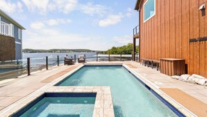 Una piscina rettangolare con bordo piastrellato, circondata da un pontile in legno e una ringhiera in vetro.