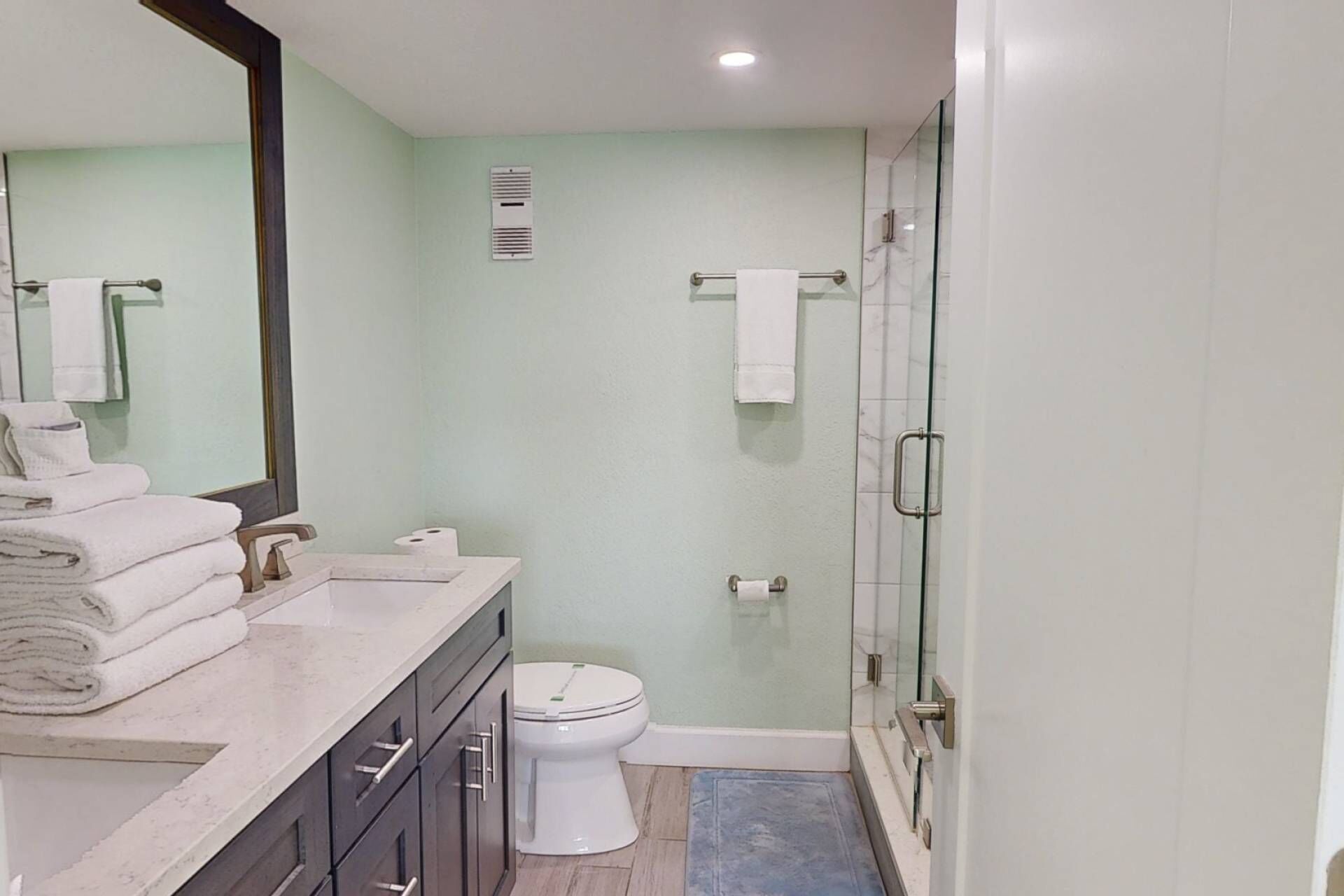 Een moderne badkamer met een glazen douchecabine, toilet en wastafel met spiegel en handdoekstapel.