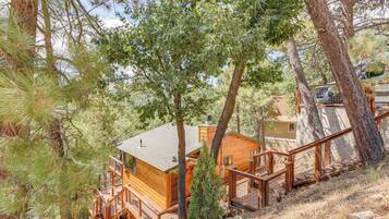Una cabaña de madera con terraza y escaleras, rodeada de árboles.