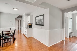 Una cocina amplia con suelo de madera, armarios blancos y un comedor con mesa y sillas.