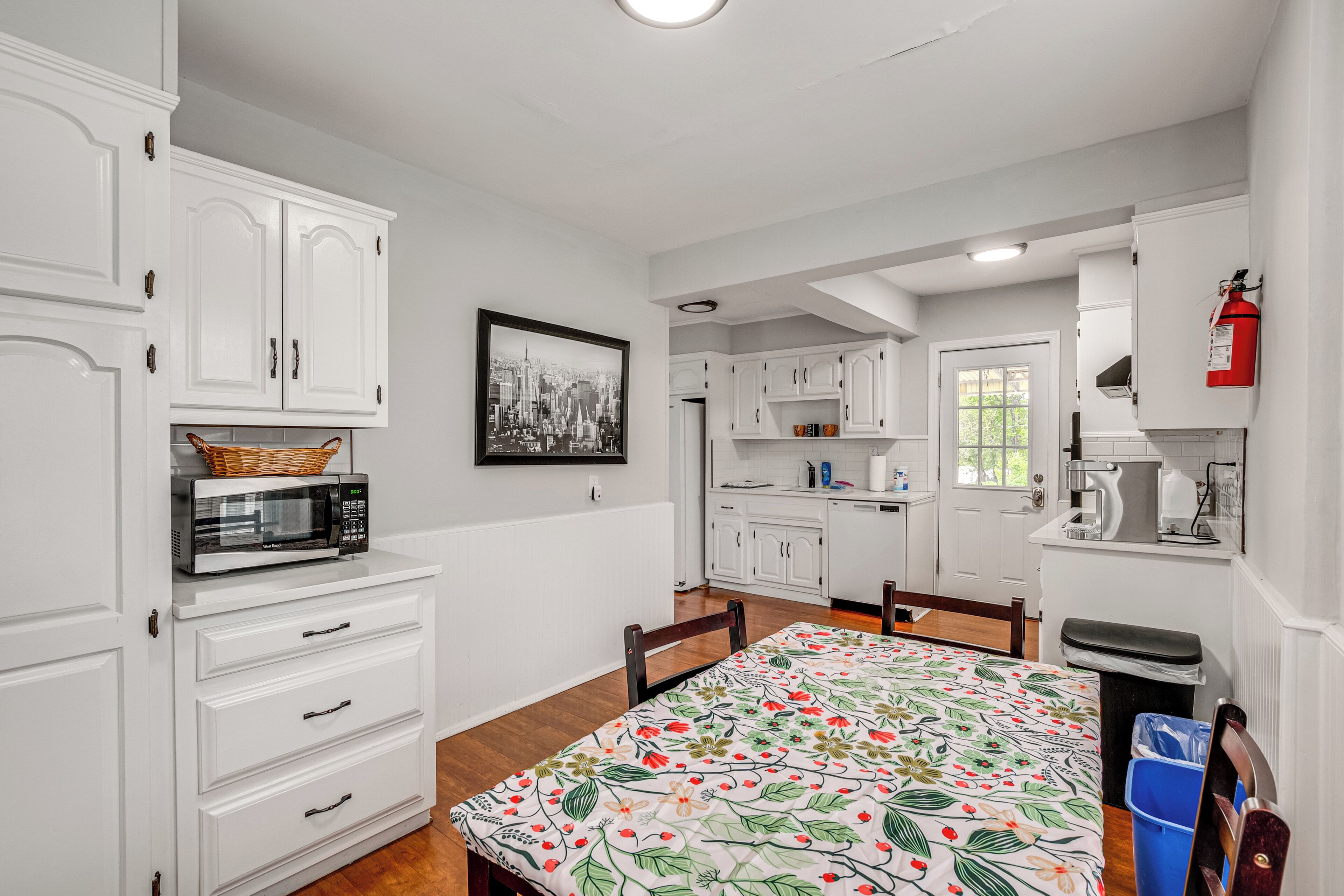 Una cocina moderna con armarios blancos, microondas y una mesa de comedor con mantel floreado.