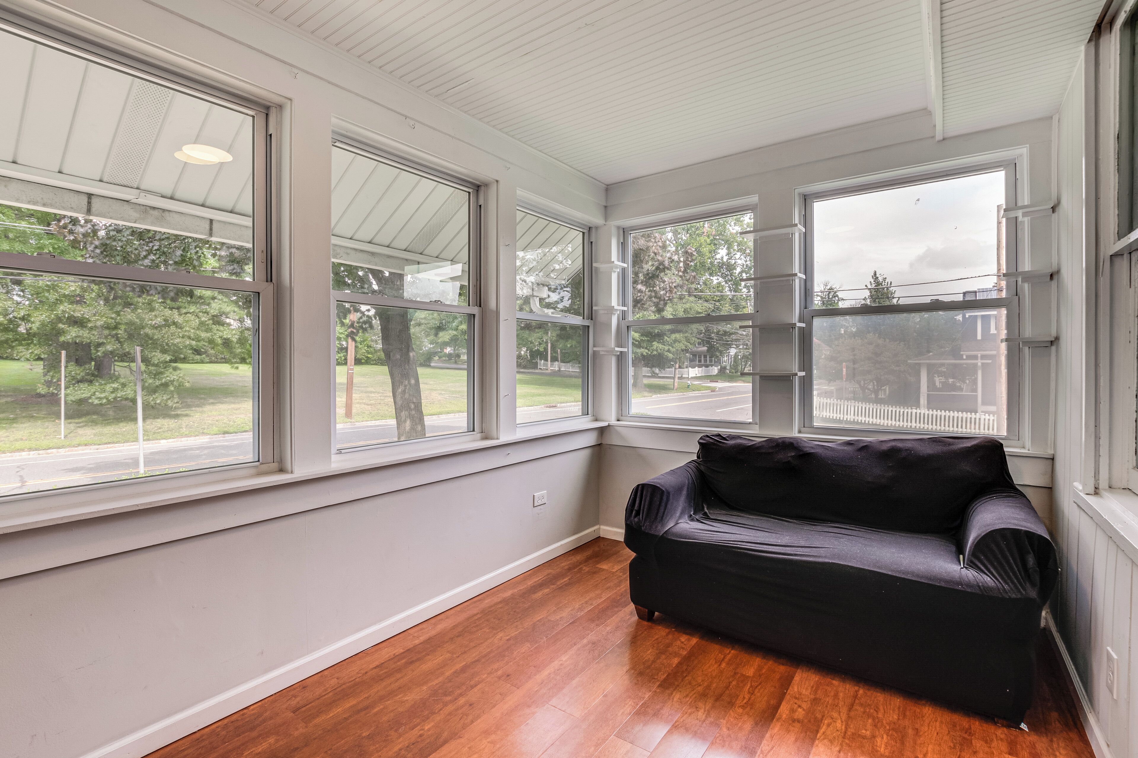 A room with large windows, a wooden floor, and a black sofa.