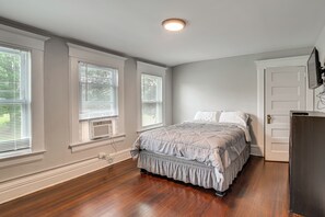 Un dormitorio con una cama, un aparador y tres ventanas con persianas.