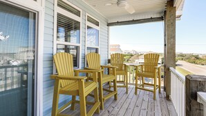 Een houten terras met vier Adirondack-stoelen, een plafondventilator en uitzicht op de oceaan.