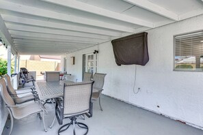 A covered patio area with a table and chairs, a window with blinds, and a brick wall in the background. - Pool, Basketball + BBQ! Glendale Group Getaway (Glendale)