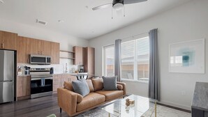 Un apartamento moderno con cocina, sala de estar con sofá y mesa de centro, y ventanas grandes con persianas.
