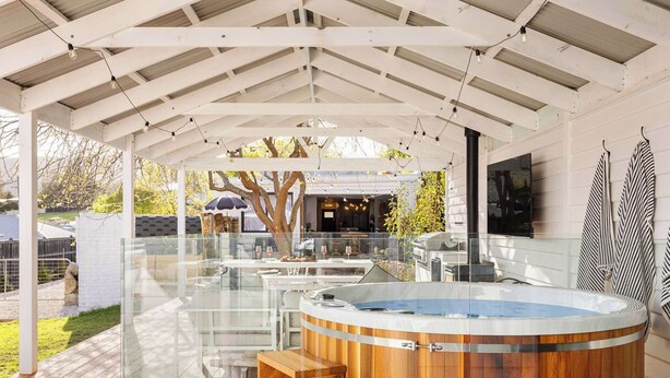A covered outdoor area with a hot tub, wooden seating, and a glass enclosure.