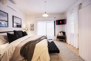 Makuuhuoneessa on sänky, penkki, tuoli, televisio ja ikkuna, jossa on verhot.