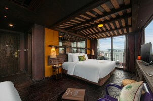 A hotel room with a large bed, a desk, a chair, a TV, and a balcony with a view.
