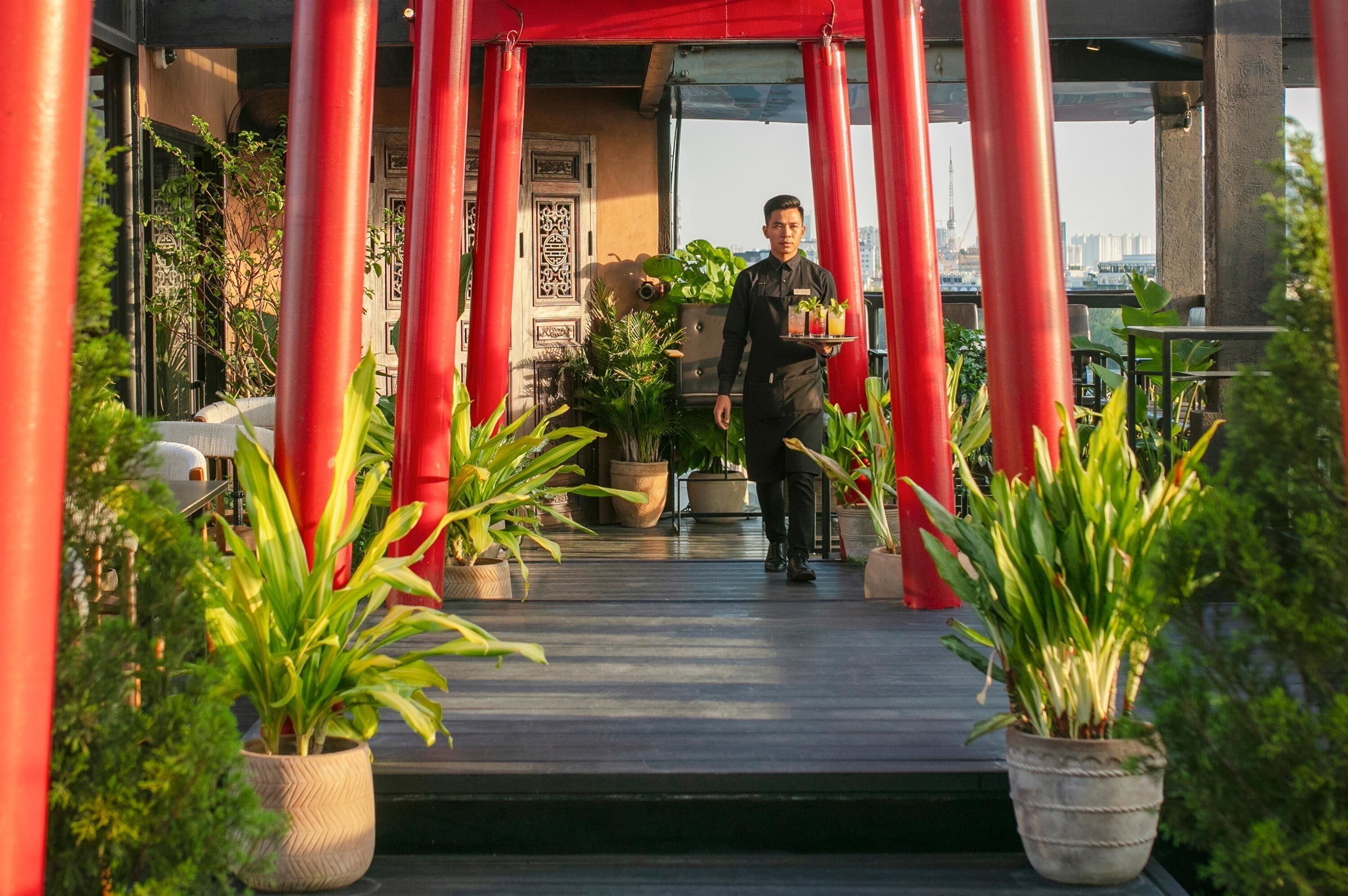 A hotel entrance with a red archway, potted plants, and a waiter carrying a tray.