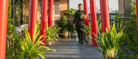 A hotel entrance with a red archway, potted plants, and a waiter carrying a tray.
