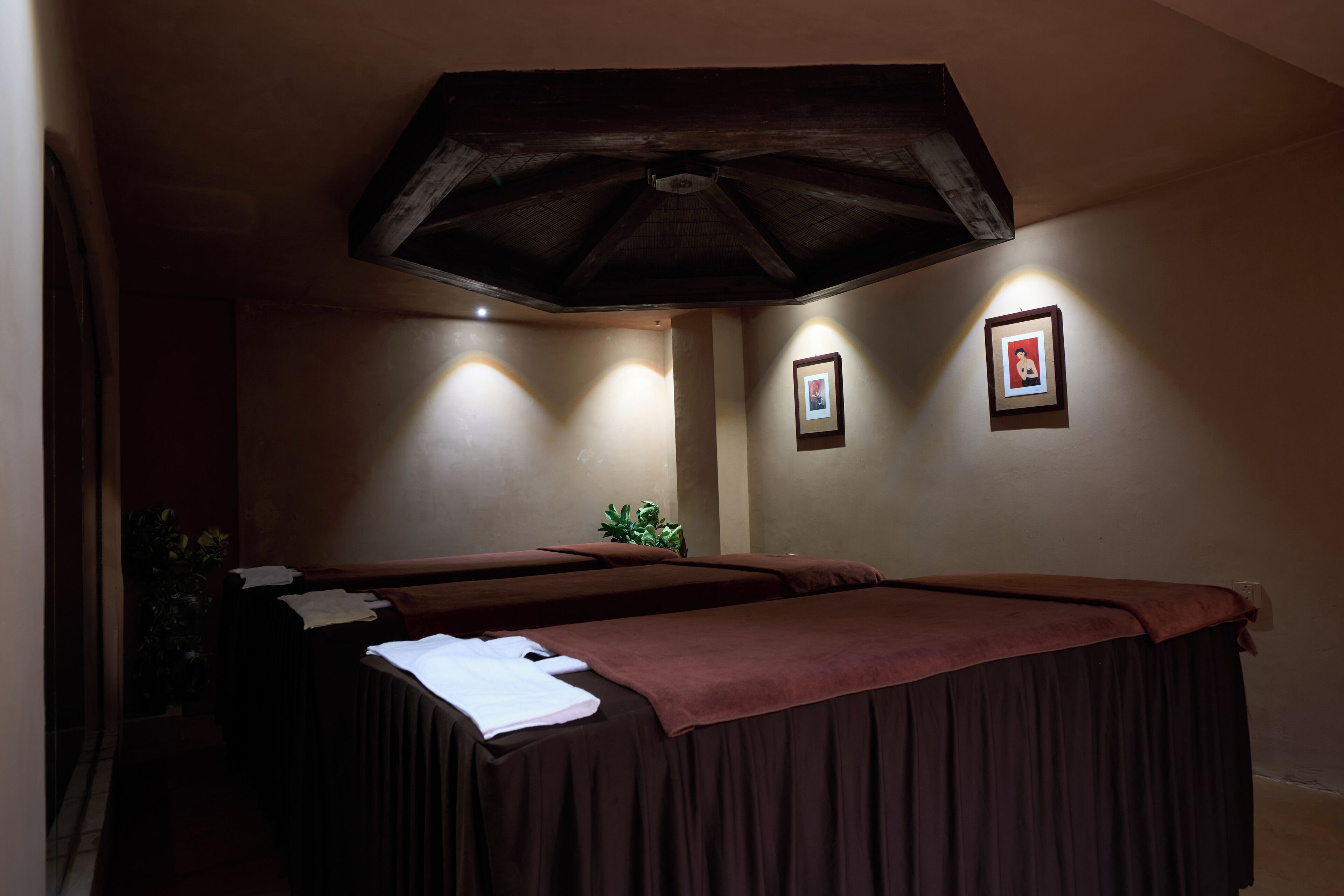 Une salle de spa équipée de deux tables de massage, d’un ventilateur de plafond et de tableaux encadrés aux murs.