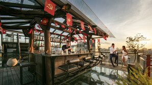Un bar en la azotea con piso de vidrio, terraza de madera y banderas rojas.