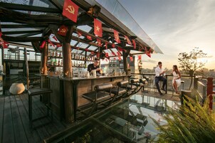 A rooftop bar with a glass floor, wooden deck, and red flags.