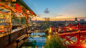 Un bar en la azotea con piscina de cristal, vistas a la ciudad y elementos estructurales rojos.