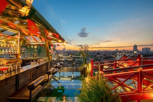 A rooftop bar with a glass pool, city views, and red structural elements.