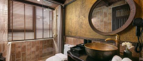 A bathroom with a wooden shower, a white toilet, a sink with a gold basin, and a round mirror.