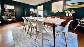Un comedor con una mesa de madera, sillas blancas y una lámpara de araña.