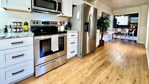 Una cocina moderna con electrodomésticos de acero inoxidable, armarios blancos y piso de madera.