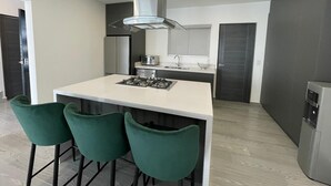 Uma cozinha moderna com ilha central, banquetas, fogão embutido e coifa de aço inoxidável.