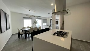 Uma cozinha moderna com uma ilha central, área de jantar com cadeiras e uma escada que leva a outro andar.
