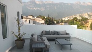 Terraço no telhado com um sofá cinzento, uma mesa de madeira e um vaso de planta.